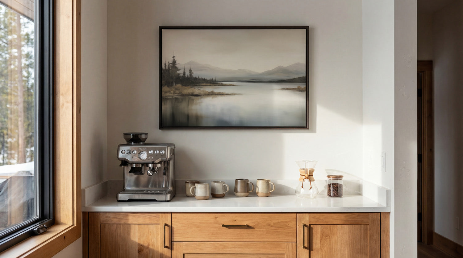 a cozy kitchen scene with a framed landscape painting on the wall above a white countertop with a coffee machine and coffee cups.