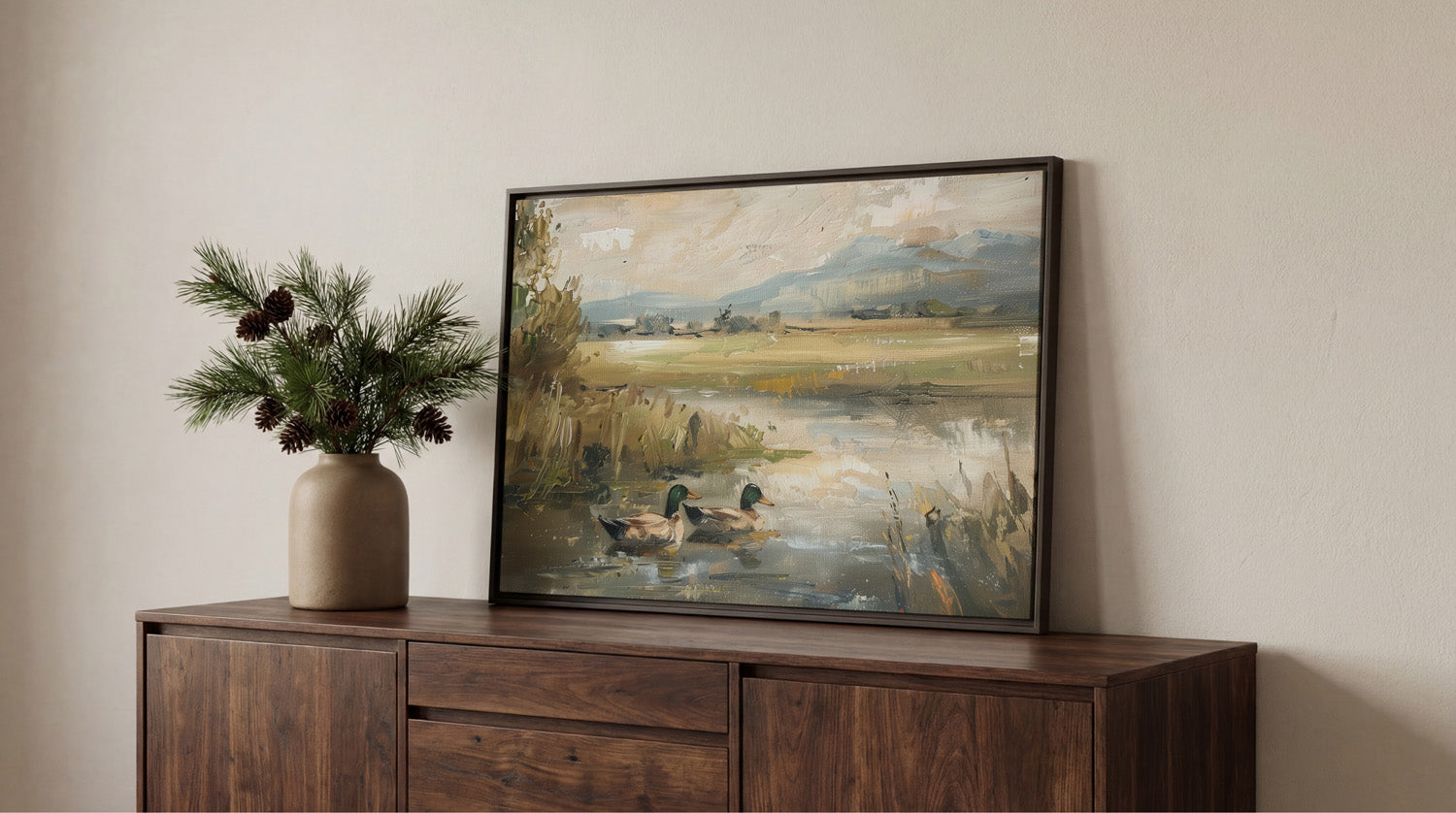 a wooden cabinet with a framed painting of ducks swimming in a pond, placed on top of it. The painting is set against a white wall, creating a serene and peaceful atmosphere.