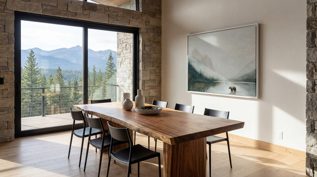 a modern dining room with a large wooden table and chairs, a large window offering a scenic view of a mountain range, and a framed landscape painting on the wall.
