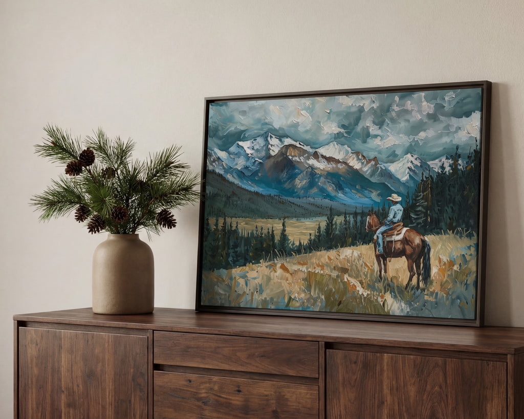 a painting of a cowboy riding a horse in a mountainous landscape, with pine trees and a vase of pine cones on a wooden cabinet.
