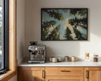 a kitchen counter with a coffee machine, coffee cups, and a framed painting of a forest scene above it.