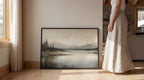 A woman in a long white skirt stands next to a framed landscape painting depicting a serene mountain scene.