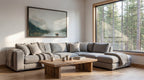 a cozy living room with a large window overlooking a forest, a wooden coffee table, and a gray sectional sofa.