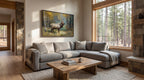 a cozy living room with a large window overlooking a wooded area. The room features a gray sectional sofa, a wooden coffee table, and a painting of a deer on the wall.