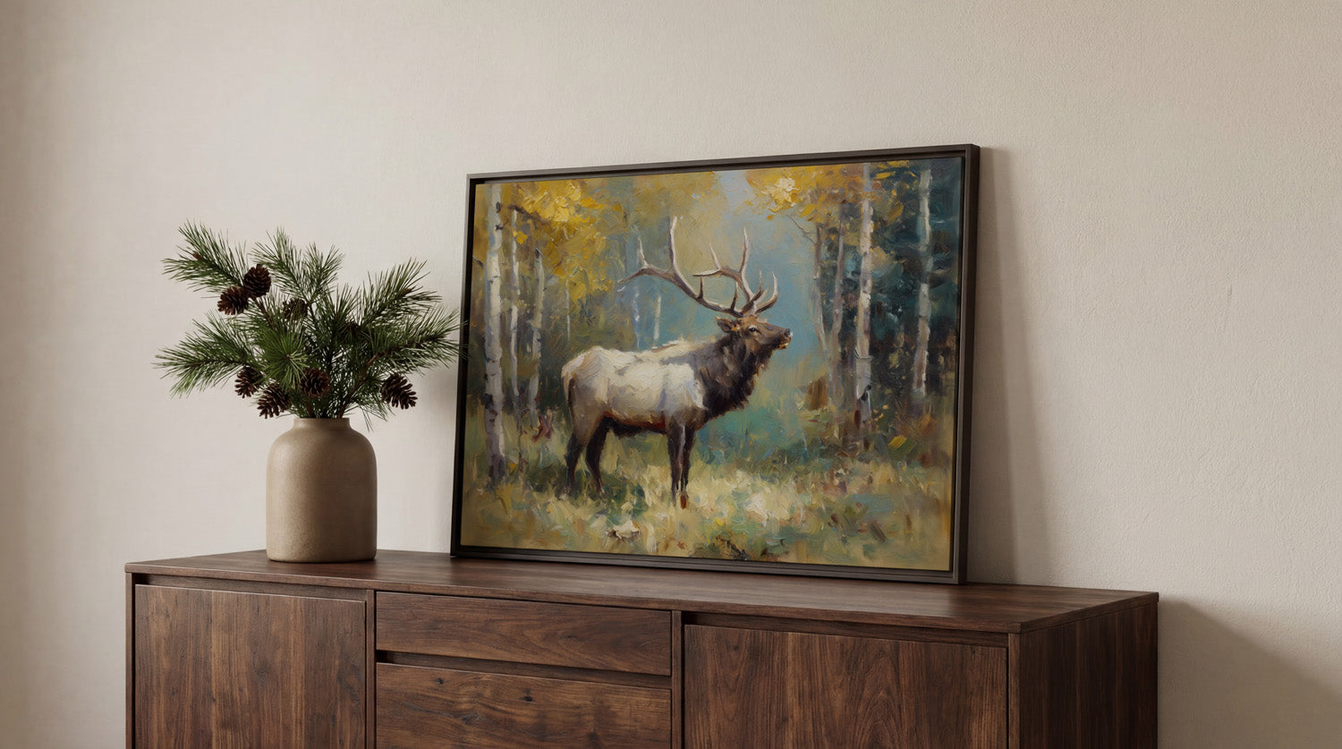 a framed painting of a majestic elk standing in a forest, with a vase of pine branches and pine cones on a wooden cabinet below it.