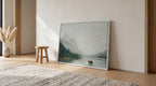 a large landscape painting depicting a serene scene of a bear standing in a lake, surrounded by mountains and trees. The painting is framed and placed on a wooden floor, with a small stool nearby. The overall setting appears to be a cozy and inviting living space.