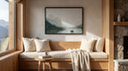 a cozy living room with a large window overlooking a scenic mountain landscape. The room features a wooden bench with plush pillows, a small wooden table with a coffee mug and a book, and a framed landscape painting hanging on the wall.