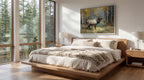 a serene bedroom with a large bed, wooden nightstands, and a painting of a deer in the background. The room has large windows that provide a view of the surrounding forest, creating a peaceful and natural atmosphere.