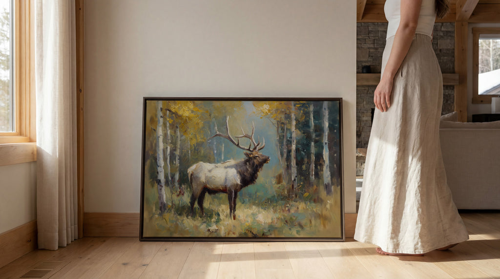 A woman in a long white skirt stands next to a framed painting of a majestic elk in a forest setting.