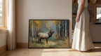 A woman in a long white skirt stands next to a framed painting of a majestic elk in a forest setting.