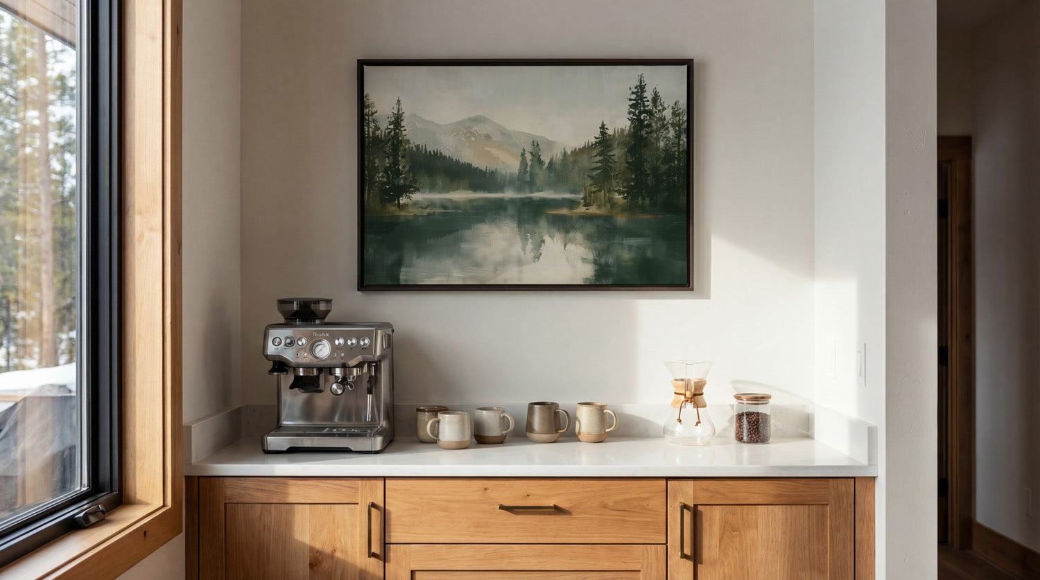 a cozy kitchen scene with a framed landscape painting hanging on the wall above a white countertop. On the countertop, there is a coffee maker and two mugs, suggesting a space for enjoying a warm beverage.