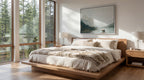 a serene bedroom with a large bed, wooden nightstands, and a painting of a mountain landscape on the wall. The room has large windows that provide a view of the surrounding trees, creating a peaceful and natural atmosphere.