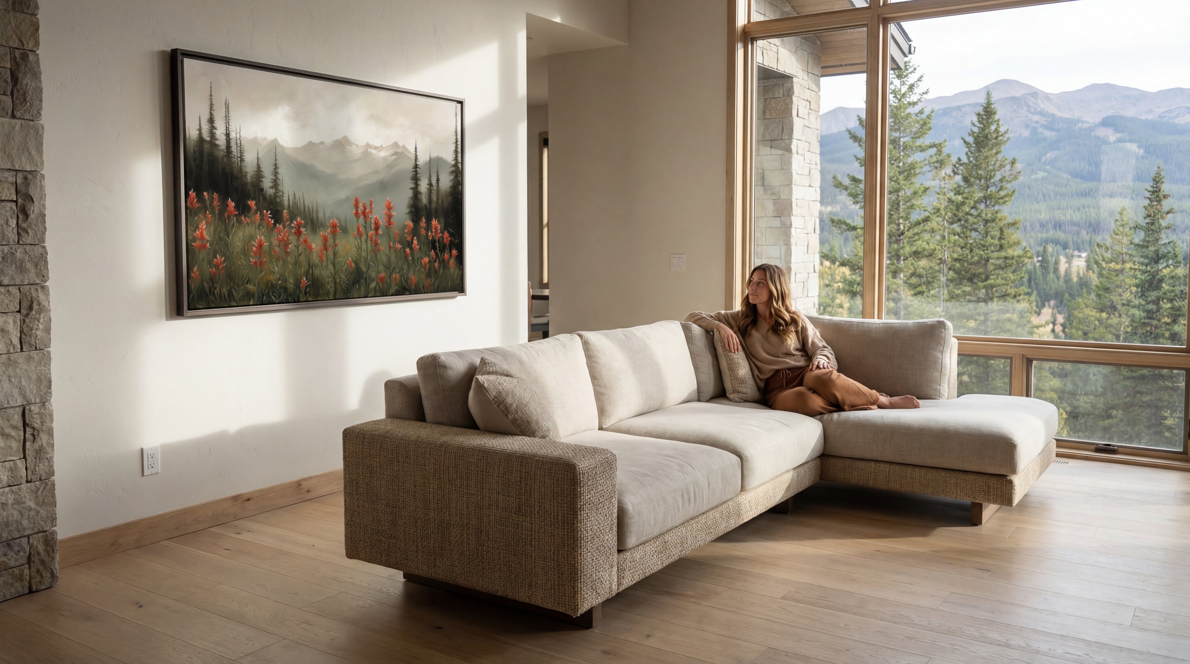 Woman sitting on a beige sectional sofa in a modern living room with large windows showing a mountain view.