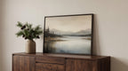 a wooden cabinet with a framed landscape painting hanging on it, placed on a white wall.