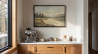 a cozy kitchen scene with a framed landscape painting hanging on the wall above a white countertop. On the countertop, there is a coffee maker and two mugs, suggesting a space for enjoying a warm beverage.
