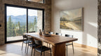 a modern dining room with a large wooden table and chairs, a painting of a mountain landscape on the wall, and a view of the mountains through a large window.