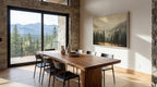 a modern dining room with a large wooden table and chairs, a large window offering a scenic mountain view, and a framed landscape painting on the wall.