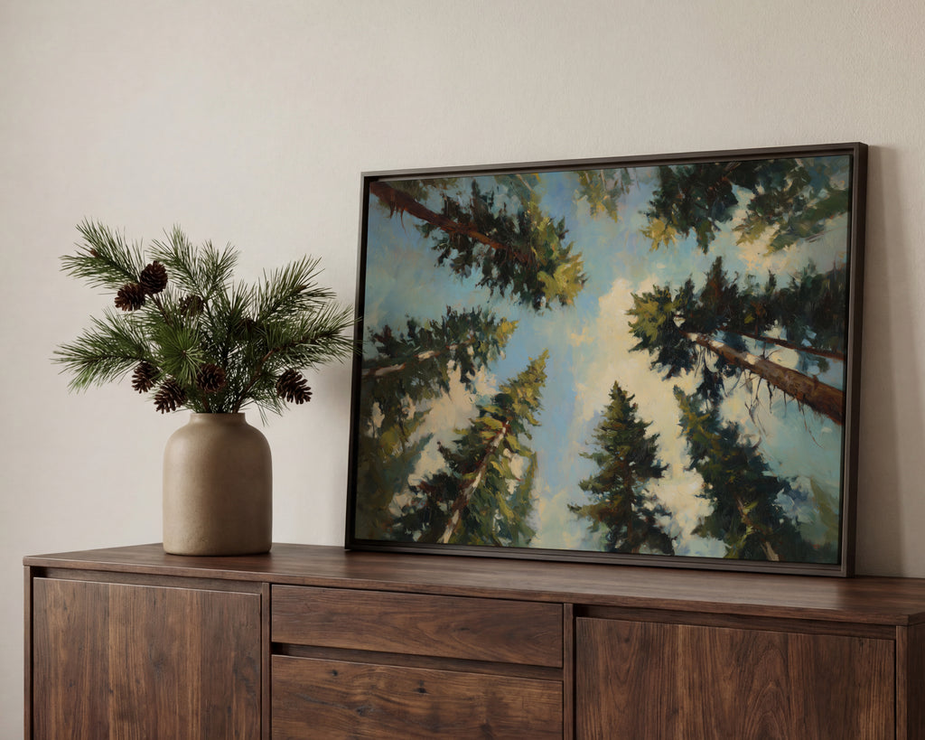 a wooden cabinet with a framed painting of pine trees hanging on it, placed on a shelf. Next to the painting, there is a vase with pine branches and pine cones.