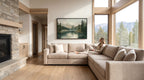 A woman sits on a beige sectional sofa in a spacious living room, with a large window offering a scenic view of a mountain landscape.