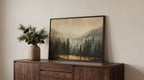 a wooden cabinet with a framed landscape painting hanging on it, depicting a serene forest scene with pine trees and a lake.