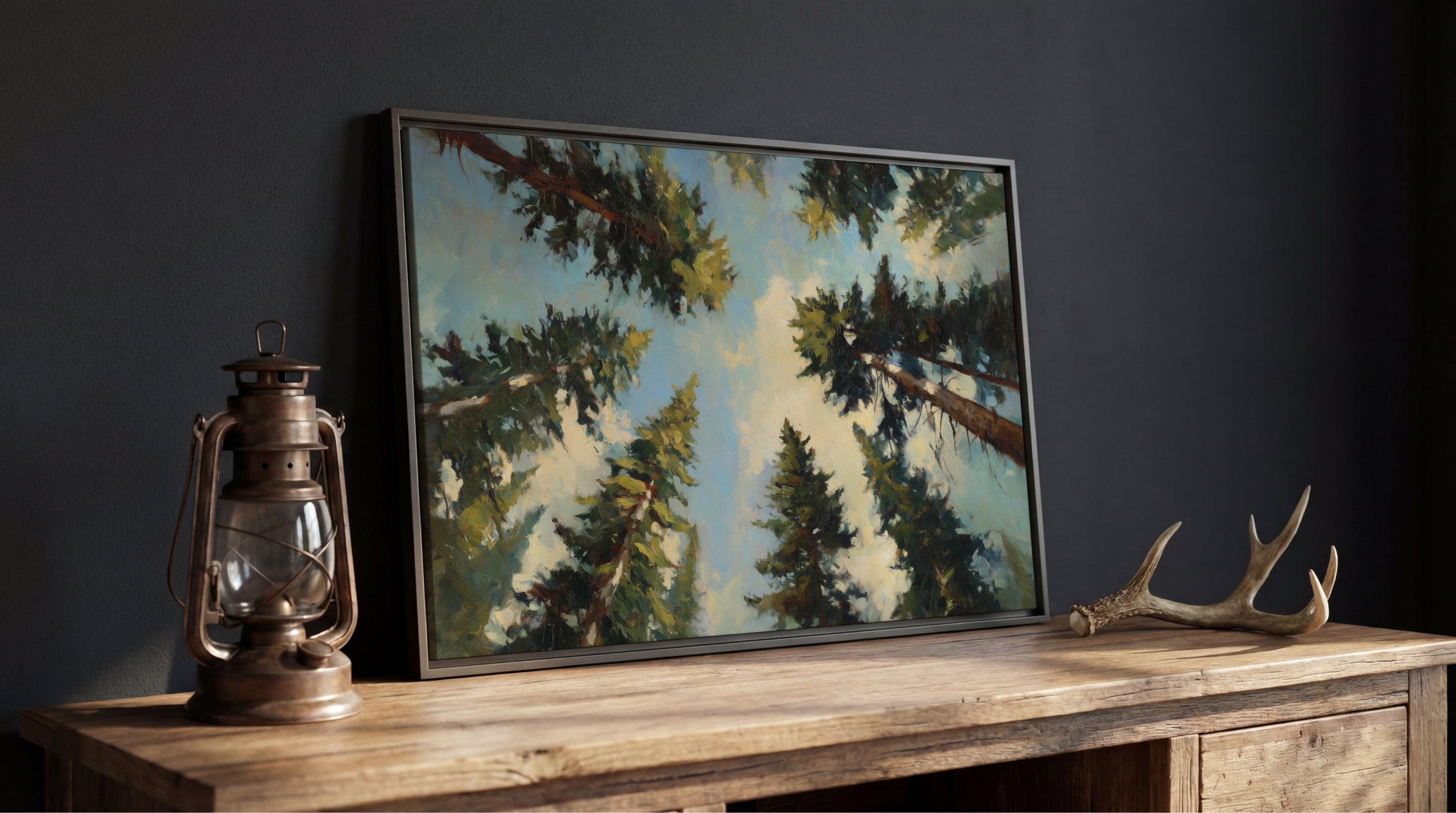 a wooden table with a framed painting of a forest scene, a lantern, and a pair of antlers.