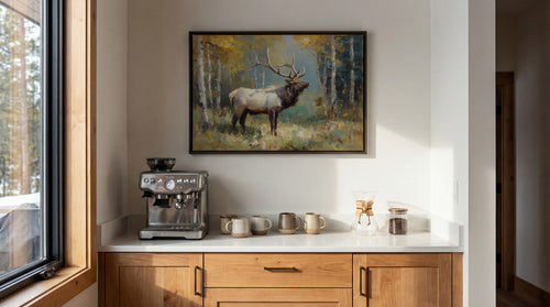a kitchen counter with a coffee maker, two mugs, and a glass jar containing what appears to be coffee beans. Above the counter, there is a framed painting of a deer in a forest setting.