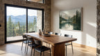 a modern dining room with a large wooden table and chairs, a framed landscape painting on the wall, and a view of mountains through a large window.